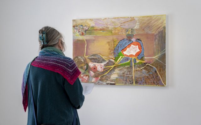 A woman is looking at a colourful painting on the wall in front of her.