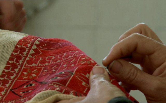 A close up of hands stitching a delicate, bright red pattern on cloth