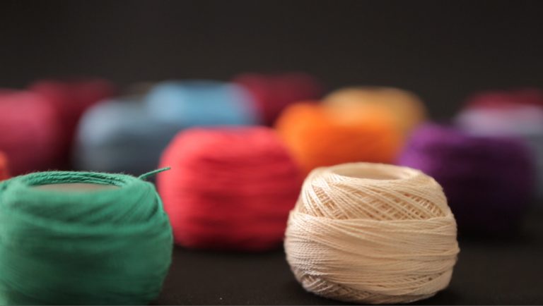 A close up image of balls of brightly coloured thread against a black backdrop.