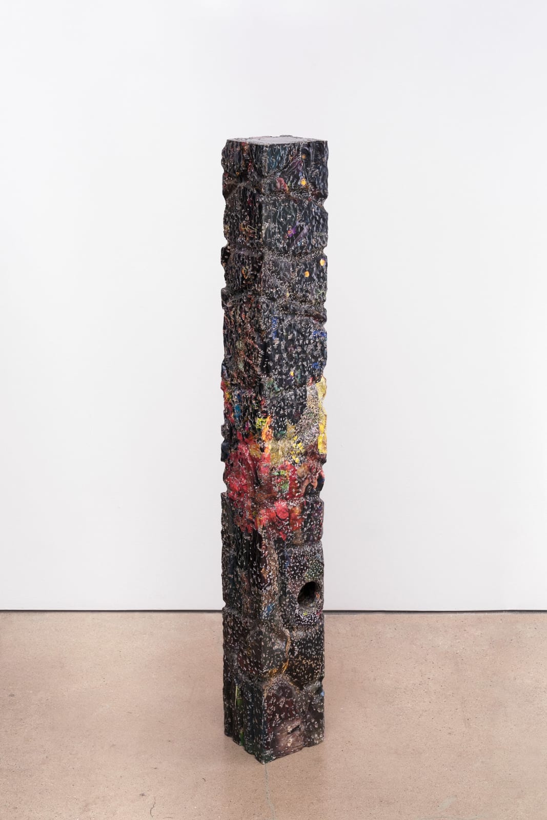 The sculpture ‘Laptower’ (2024) by Anderson Borba. The art piece is roughly the size and height of a wide fence post and is mostly coloured black and very dark blue. In the middle of the post, the colouring changes to yellow and red in a shape which resembles coral. There are a multitude of small white markings resembling fungi or coral that grow on sunken ships and underwater objects.