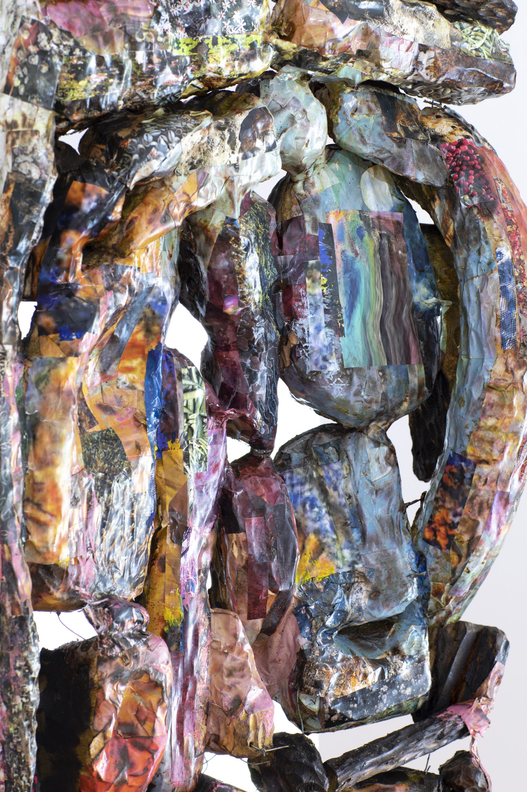 A colourfully detailed show of Anderson Borba's artwork 'Cloak' (2026). Textured pieces of wood are covered in abstract colourful details, created using collaged pieces of magazine pages. The pieces are connected together with wire and are suspended in the air.